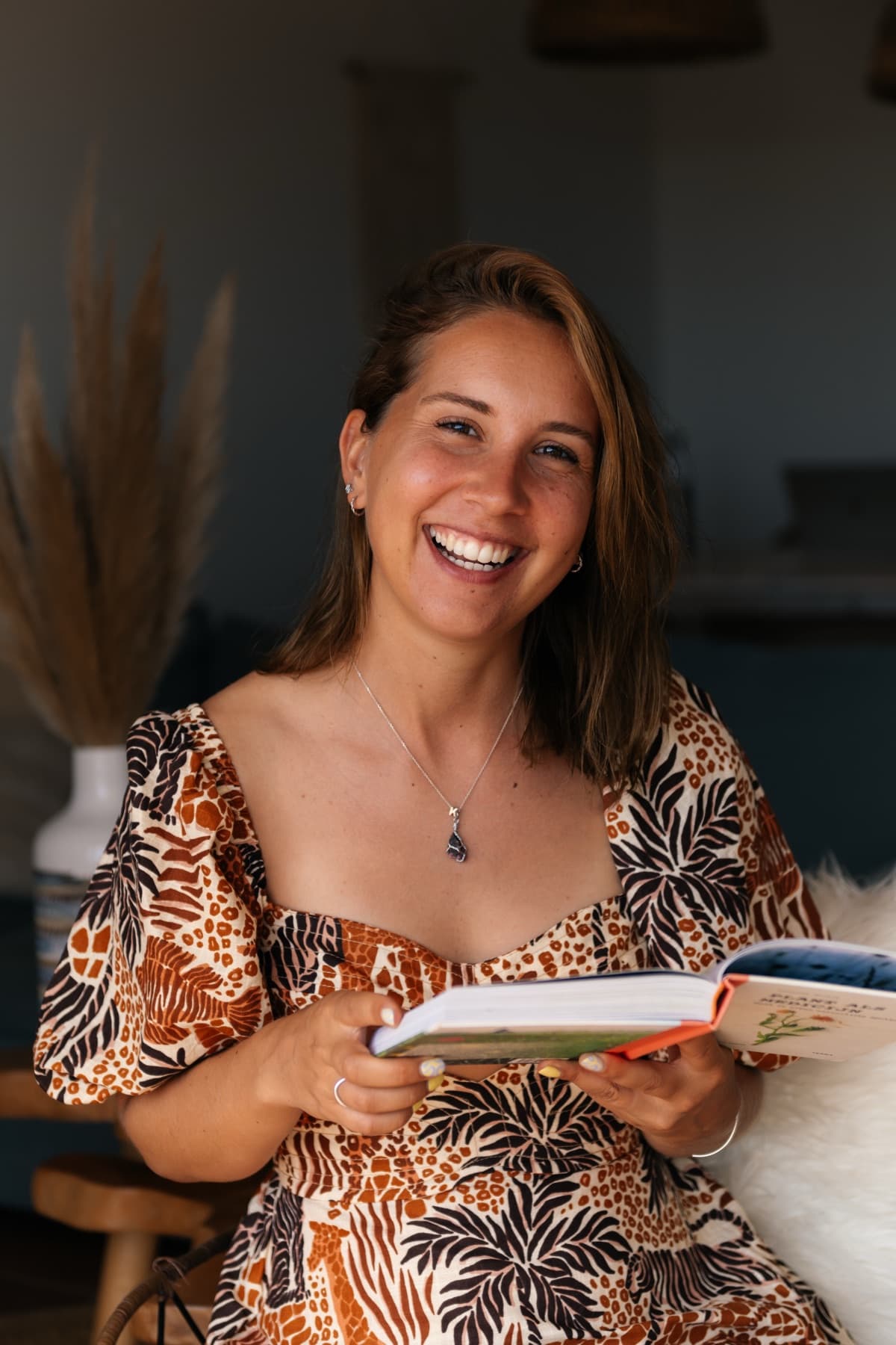 Kristel kijkt lachend in de camera met een open boek in haar handen