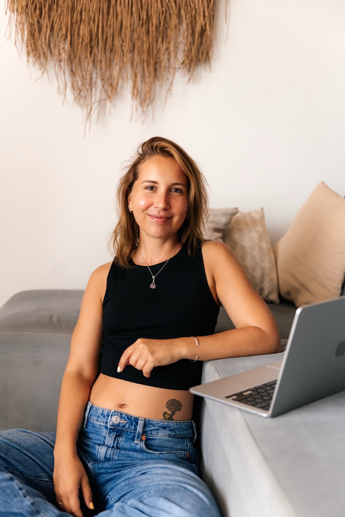 Kristel glimlacht in de camera, zittend naast een laptop op de bank